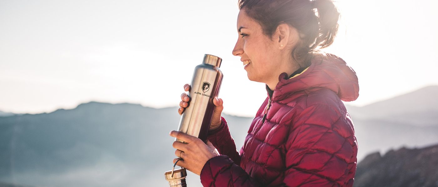 Eine Frau in rotem Mantel hält eine Wasserflasche, im Freien, ideal für Bergwanderungen und Naturerkundungen.