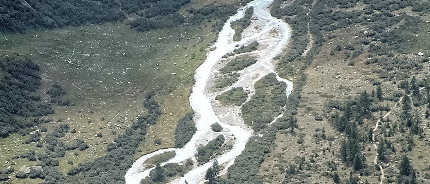 Luftaufnahme eines Flusses, der durch ein grünes Tal fließt, passend zur Outdoor-Ausrüstung von Alpinloacker für Wander- und Naturerlebnisse.