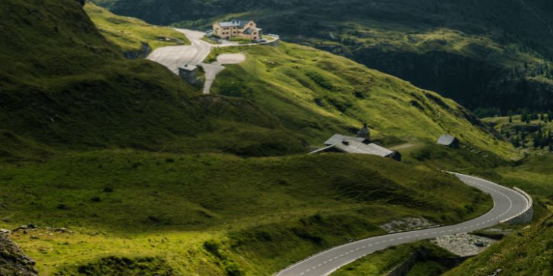 Eine Straße führt zu einem Haus auf einem grünen Hügel, umgeben von Natur, die Outdoor-Abenteuer symbolisiert.