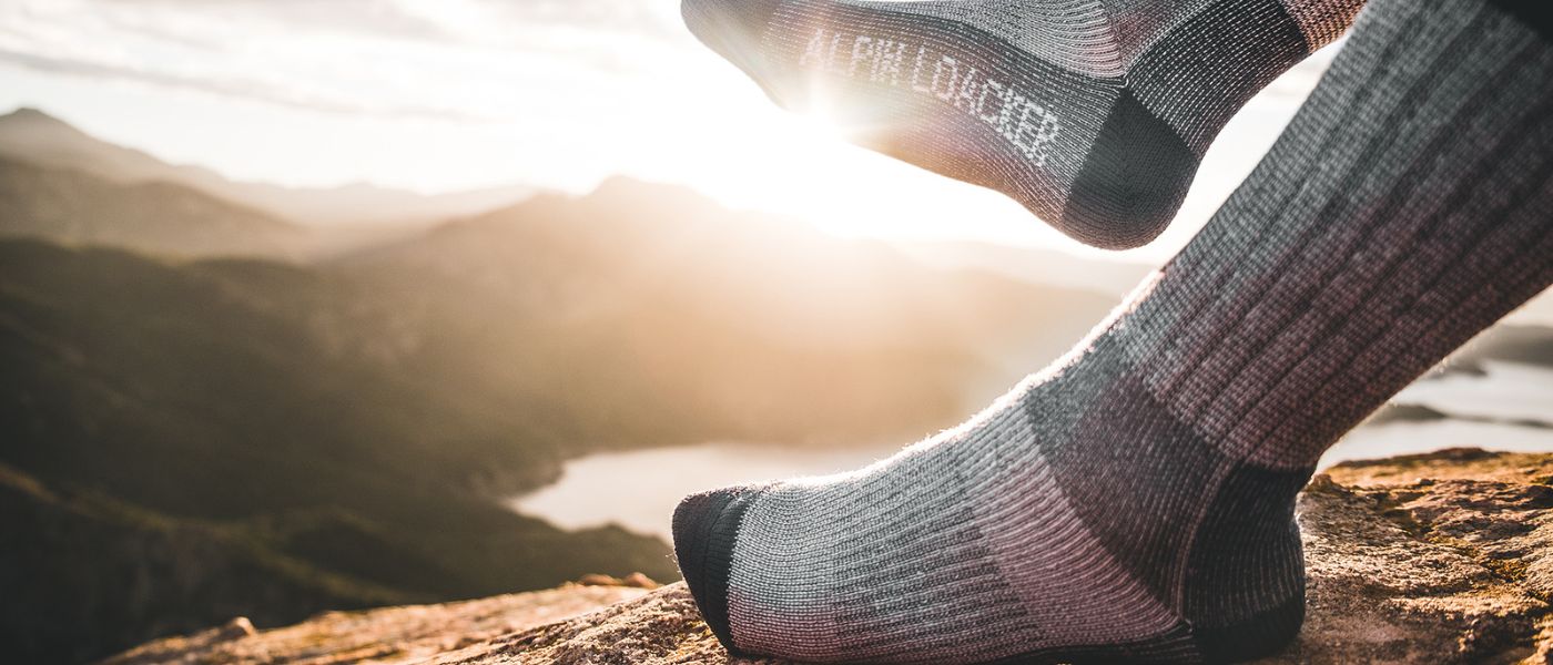 Nahaufnahme eines Fußes in einem Outdoor-Socken auf einem Felsen mit Blick auf einen See, passend für Outdoor-Aktivitäten.