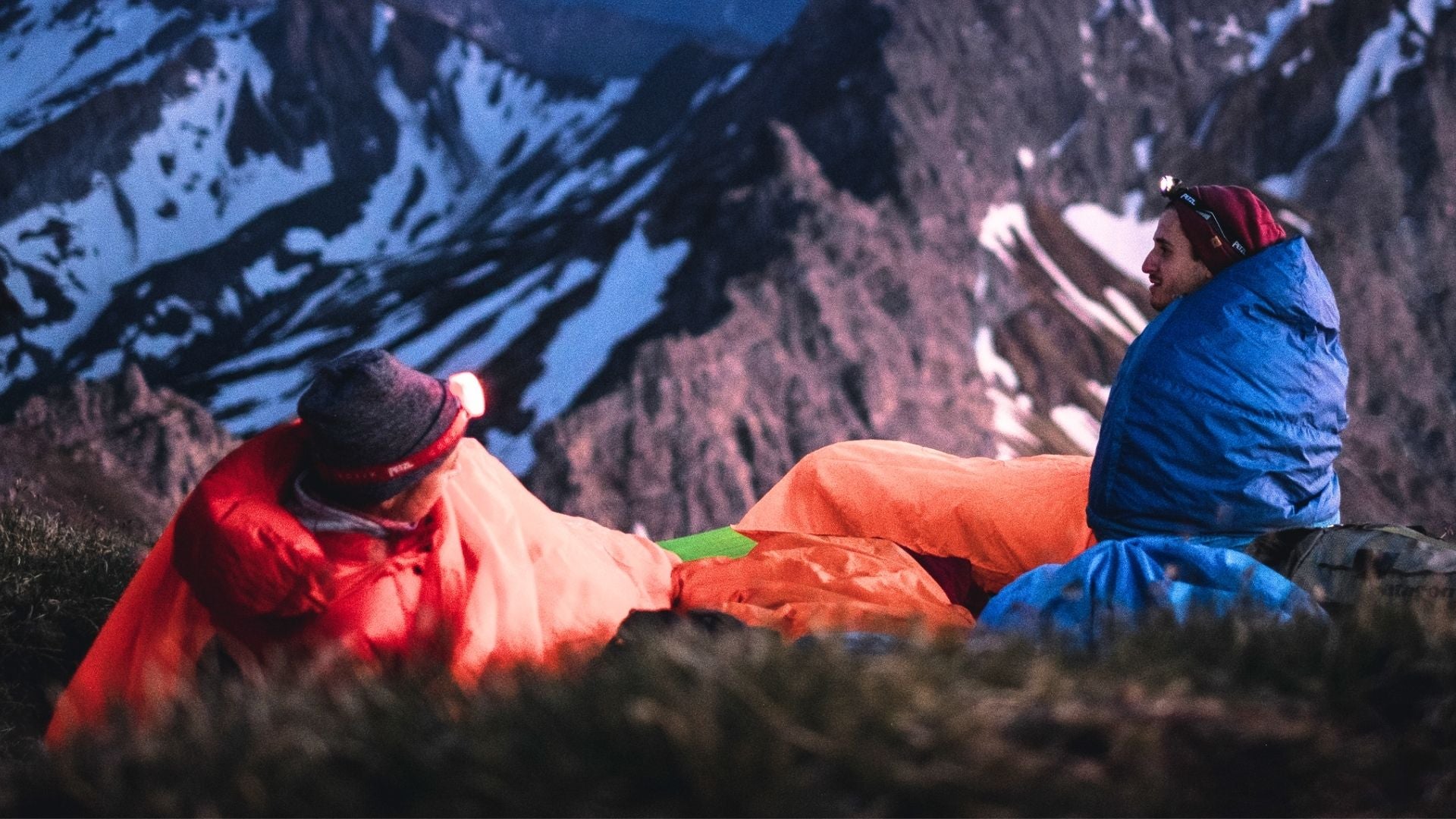 Zwei Personen liegen in Schlafsäcken auf einem Berg, passend für Alpinloacker's Outdoor-Angebote wie Schlafsäcke und Merino-Kleidung.