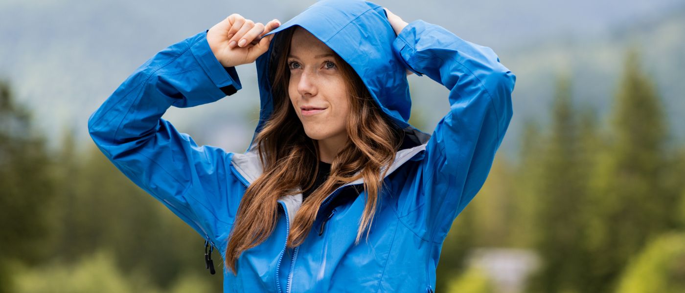 Eine Frau trägt eine blaue Regenjacke, passend für Outdoor-Aktivitäten, perfekt für das Sortiment von Alpinloacker, spezialisiert auf Outdoor-Ausrüstung.