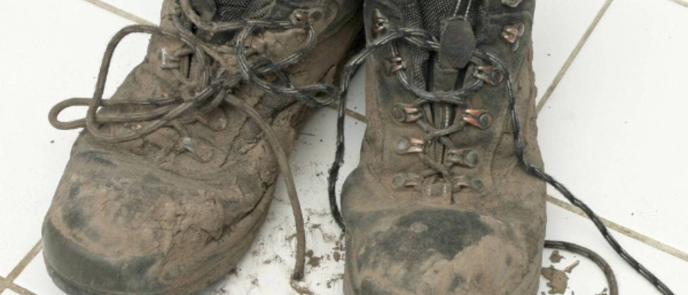 Nahaufnahme eines dreckigen Wanderstiefels mit Schnürsenkel auf weißem Untergrund, passend für Outdoor-Aktivitäten.