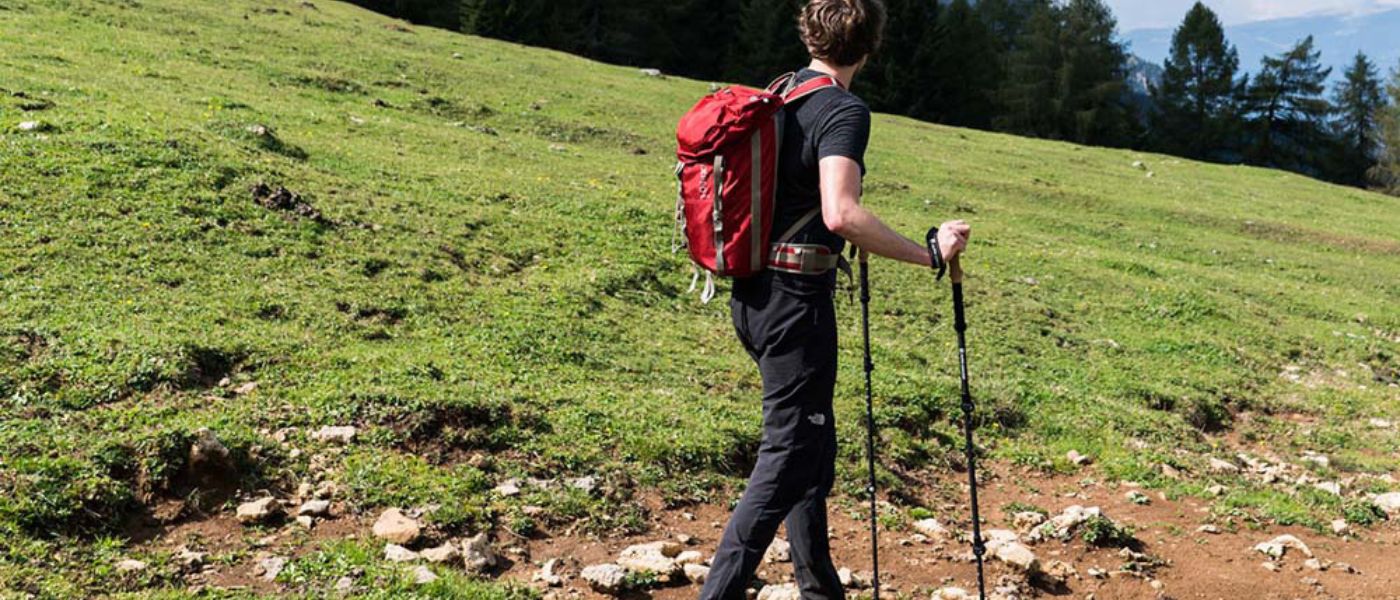 Ein Mann mit Rucksack und Wanderstöcken wandert auf einem Hügel, repräsentiert Outdoor-Aktivitäten und Ausrüstung von alpinloacker.com.