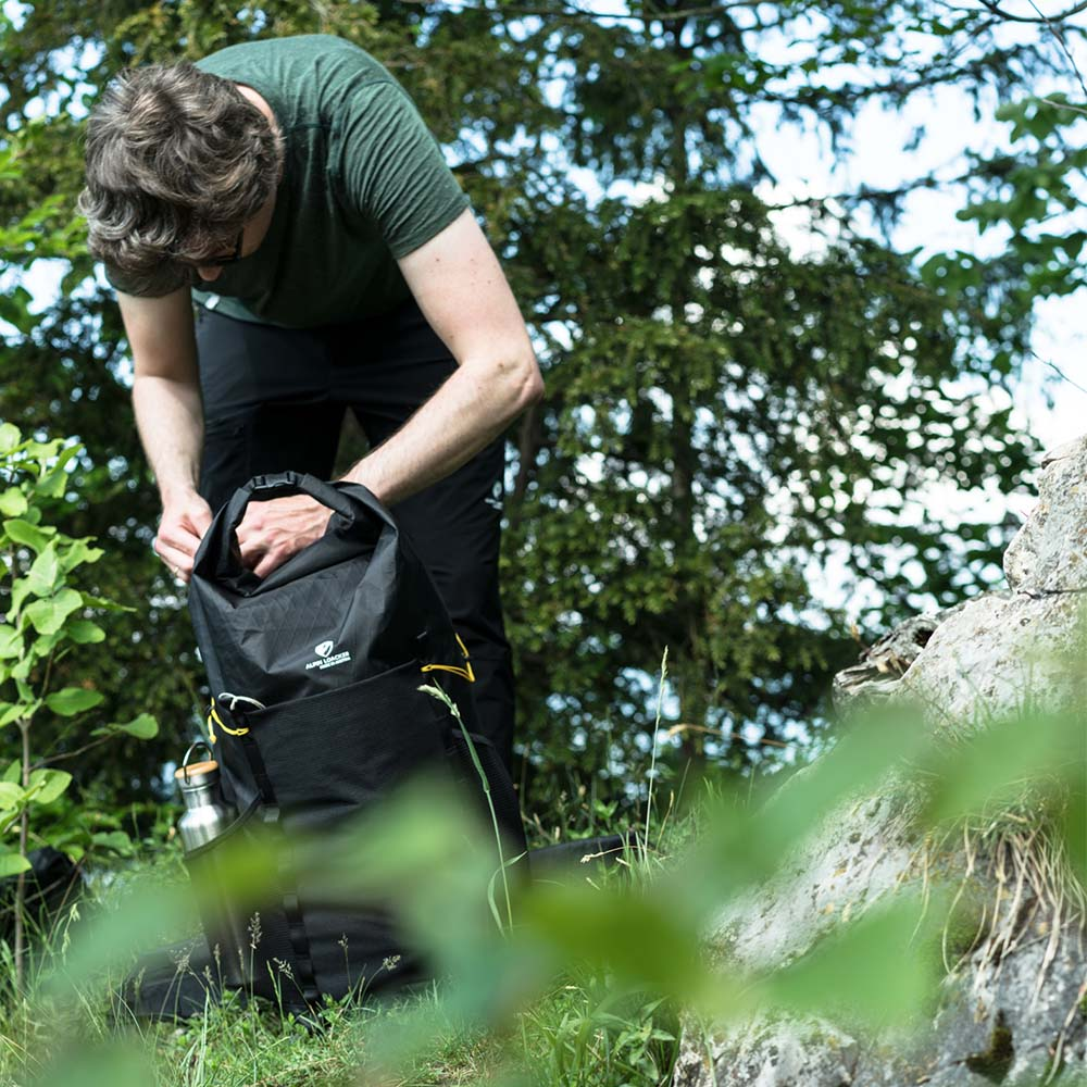 Ein Mann betrachtet einen Rucksack im Freien, passend für Outdoor-Aktivitäten wie Wandern, im Einklang mit Alpinloacker's Sortiment.