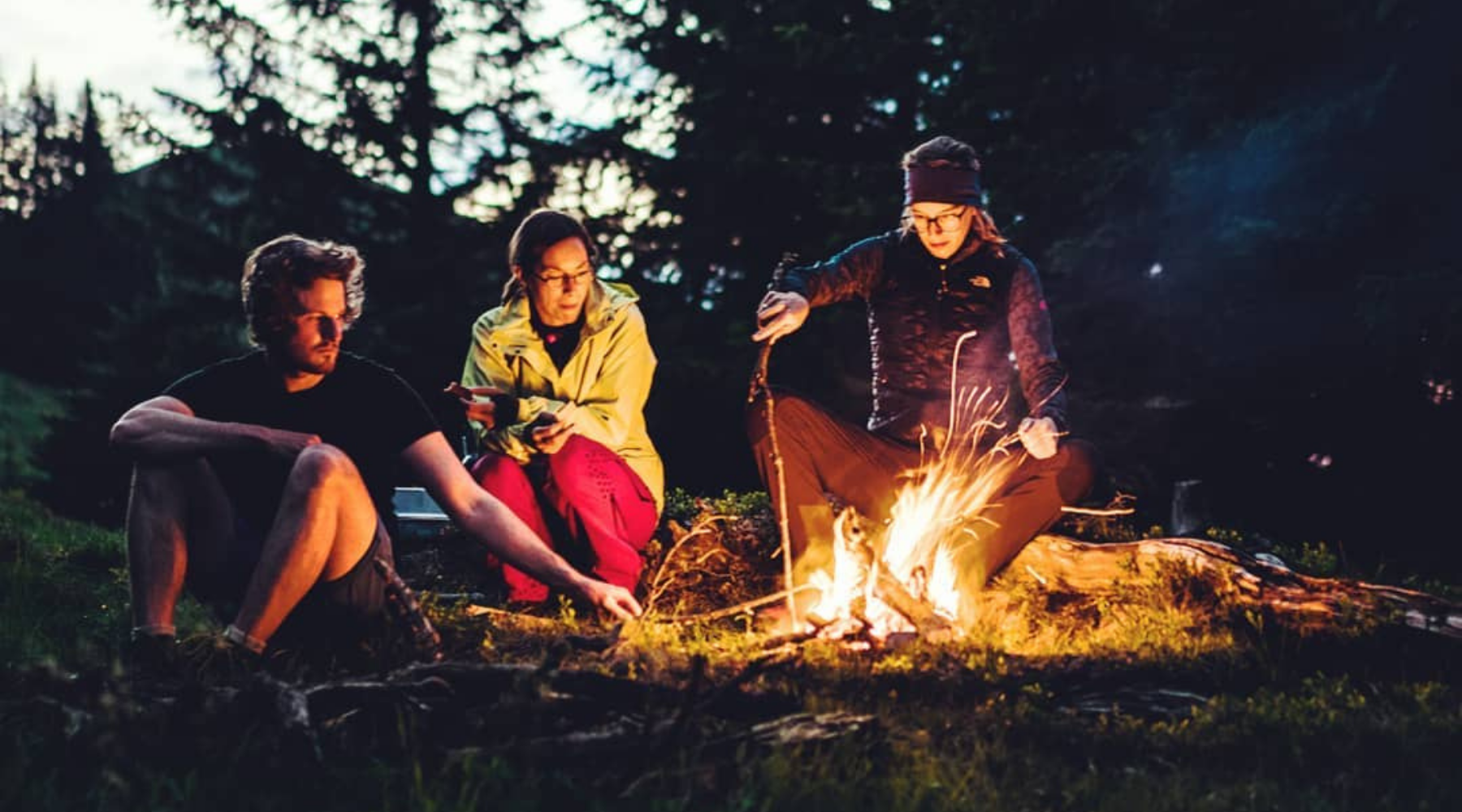 Eine Gruppe von Menschen sitzt um ein Lagerfeuer, eine Person trägt eine gelbe Jacke – passend für Outdoor-Aktivitäten.
