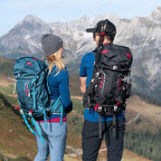 Zwei Wanderer mit 35-Liter Wanderrucksäcken von Alpin Loacker auf alpinem Pfad, umgeben von Wald und Bergen. Ideal für Outdoor-Abenteuer.