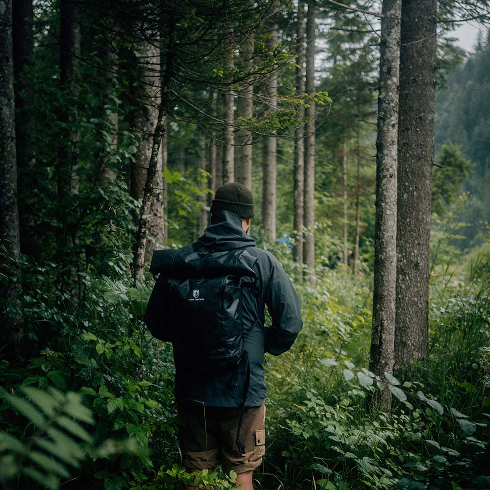 Wanderer im Wald mit leichtem, wasserdichtem Rucksack Lotus 25, ideal für Outdoor-Abenteuer, trägt Regenjacke und Beanie, umgeben von dichtem Grün.