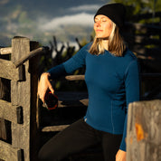 Eine Dame steht am Zaun in ihrem 230g Merino Set von Alpin Loacker. Das Oberteil ist blau.