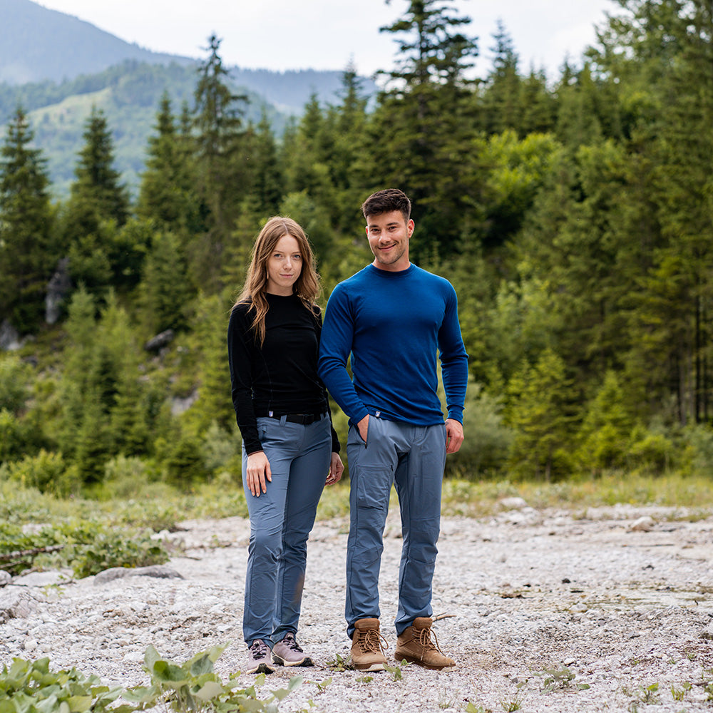 Pärchen in Outdoor-Kleidung auf Lichtung; er trägt die Softshell Wanderhose Herren, ideal für Trekking mit leichtem, elastischem Material und praktischen Taschen.
