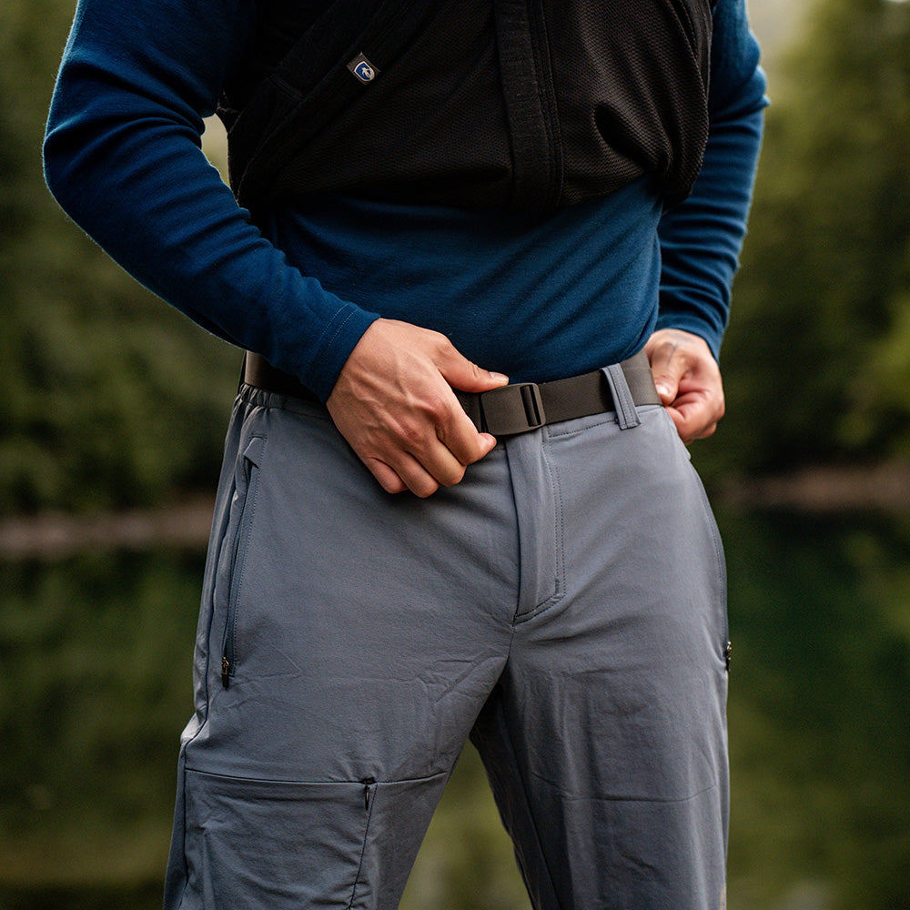 Nahaufnahme der Softshell Wanderhose Herren beim Anpassen eines schwarzen Gürtels an hellgrauer Trekkinghose; ideal für Outdoor-Abenteuer mit leichtem, elastischem Material und sportlichem Schnitt.