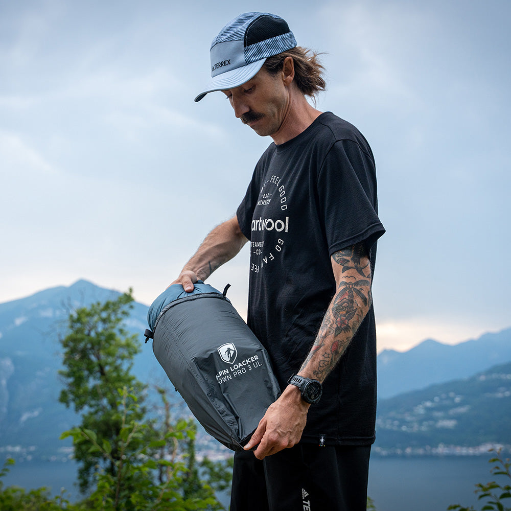 Mann am See mit Alpin Loacker Drybag Ultraleicht, hält ultraleichten, wasserdichten Packsack, ideal für Outdoor-Aktivitäten, vor Bergkulisse.