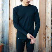 Mann trägt das 100% Merinowolle Set schwarz von Alpin Loacker vor einer Holzwand, perfekt als Baselayer für die kalte Jahreszeit