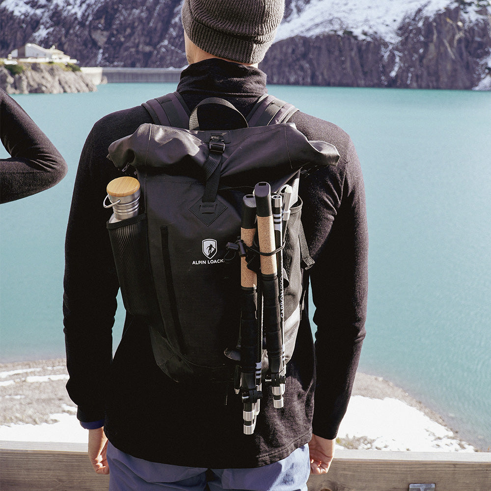 Person mit Alpin Loacker Faltbare Trailrunning Stöcke aus Carbon, blickt auf türkisfarbenen See und Berge. Stöcke am Rucksack befestigt, ideal für Outdoor-Abenteuer.