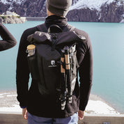 Person mit Alpin Loacker Faltbare Trailrunning Stöcke aus Carbon, blickt auf türkisfarbenen See und Berge. Stöcke am Rucksack befestigt, ideal für Outdoor-Abenteuer.