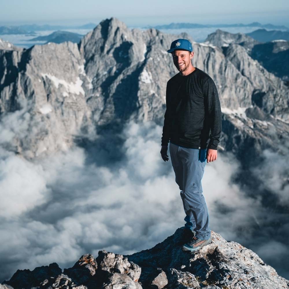 Ein Wanderer auf einem Gipfel trägt die Softshell Wanderhose Herren, die leichten Schutz und Flexibilität für alpine Abenteuer bietet.