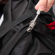 Hand zieht am Metallreißverschluss des Alpin Loacker 35-Liter Wanderrucksacks, sichtbar sind schwarze Stoffstruktur und roter Akzent. Ideal für Outdoor-Abenteuer.