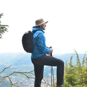 Hiker mit Leichter Rucksack wasserdicht auf Bergvorsprung, blickt ins Tal. Trägt Trekkingstöcke, ideal für Abenteuer, robust und geräumig.