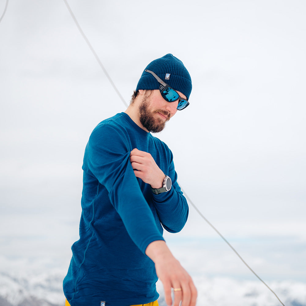 Mann im Schnee trägt das Merino Langarmshirt Herren 230 g/m2, ideal für Outdoor-Aktivitäten dank atmungsaktiver, geruchsneutraler Merinowolle.