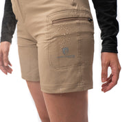Kurze Wanderhose Damen: Nahaufnahme einer wasserabweisenden, hell-khakifarbenen Shorts mit Reißverschlusstasche und sichtbar abperlendem Wasser, getragen von einer Person.