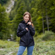 Junge Frau in Wald mit 3 Lagen Damen Hardshell Regenjacke, ideal für Outdoor-Aktivitäten, trägt Helm-kompatible Kapuze und verstellbaren Kragen, zeigt Vielseitigkeit und Schutz.