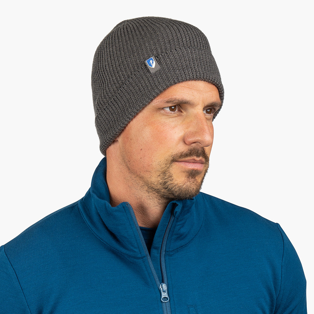 Mann trägt Merino Mütze Herren & Damen Strick 230g/m² in Anthrazit, ideal für Outdoor-Aktivitäten, kombiniert mit blauem Pullover. Ideal für jede Jahreszeit.