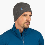 Mann trägt Merino Mütze Herren & Damen Strick 230g/m² in Anthrazit, ideal für Outdoor-Aktivitäten, kombiniert mit blauem Pullover. Ideal für jede Jahreszeit.