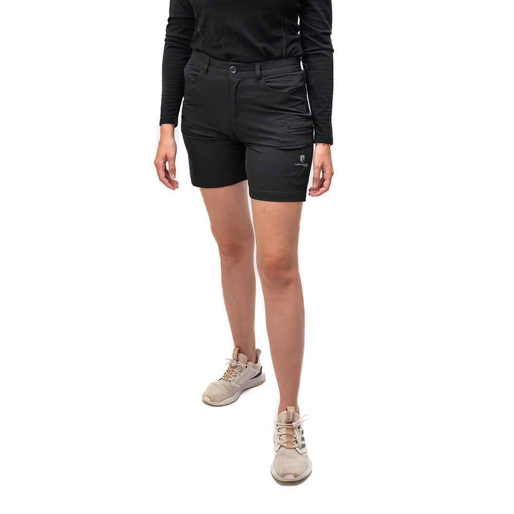 Person trägt Kurze Wanderhose Damen: schwarze, mittellange Shorts mit Stretch, Knopf-Zip-Verschluss und Logo links. Kombiniert mit schwarzem Langarmshirt und beigen Sneakers. Ideal für Outdoor-Aktivitäten.