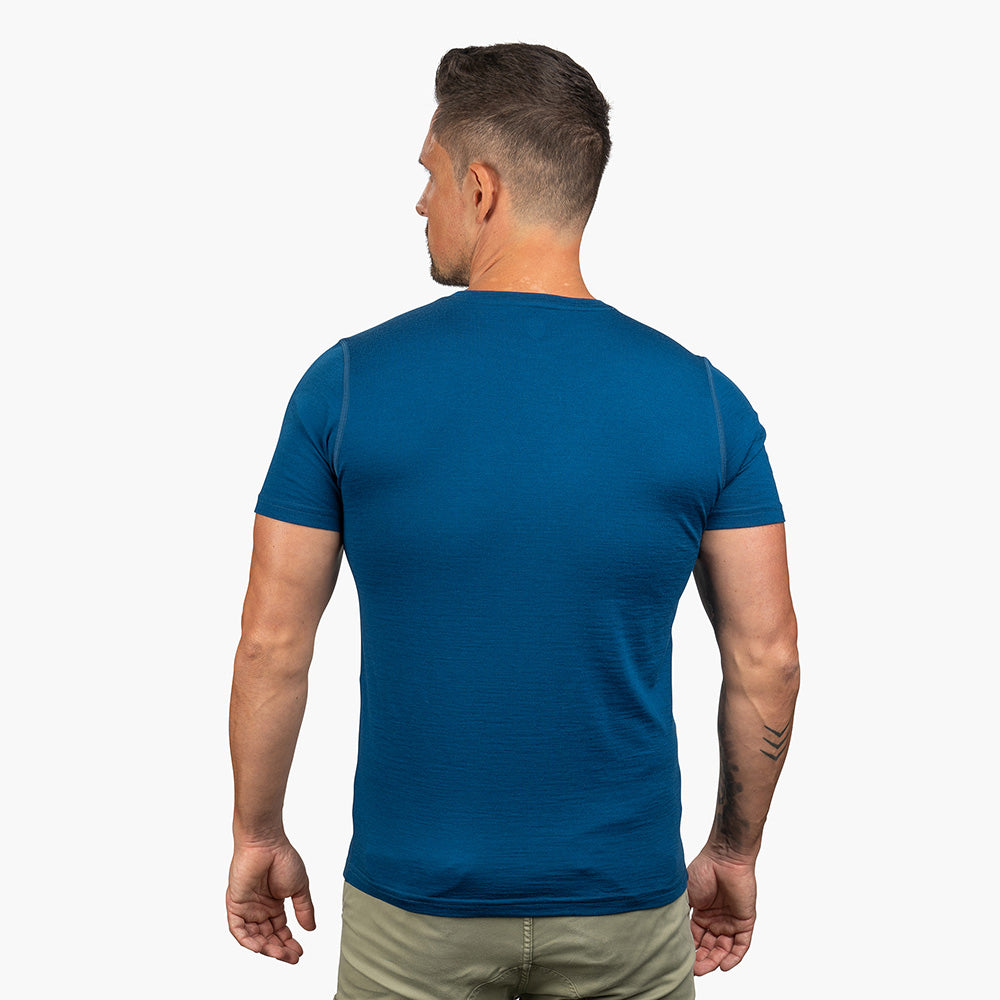 Rückansicht eines Mannes im 100% Merino T-Shirt Herren 180 g/m2, ideal für Outdoor-Aktivitäten, mit entspannten Armen, zeigt ein kleines Tattoo am Unterarm.