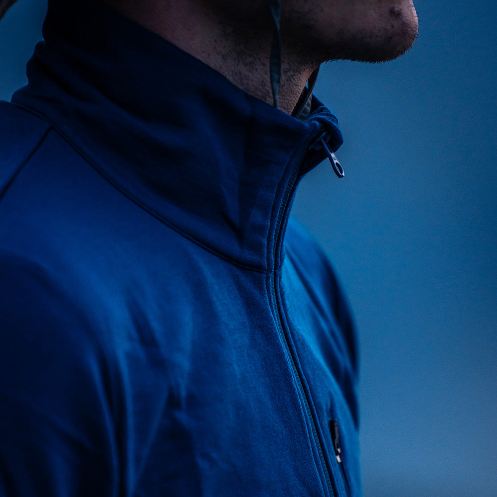 Nahaufnahme einer Person mit gestoppeltem Kinn, die eine Merino Jacke Herren 270 g/m² trägt. Ein dünnes Kabel verläuft neben dem hochgeschlossenen, blauen Kragen.