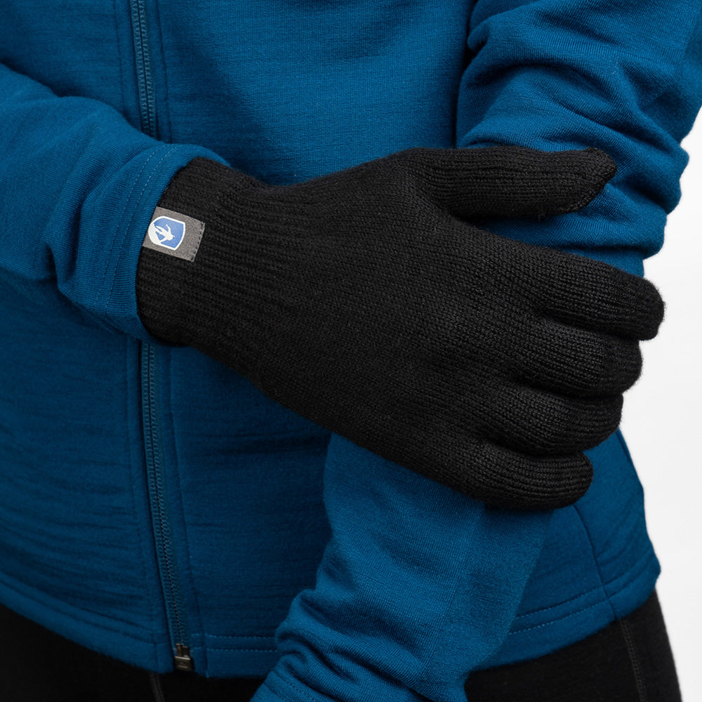 Person mit verschränkten Armen trägt blaue Jacke und einen schwarzen Alpin Loacker Merino Handschuh. Perfekt für Outdoor-Abenteuer und urbanen Alltag.