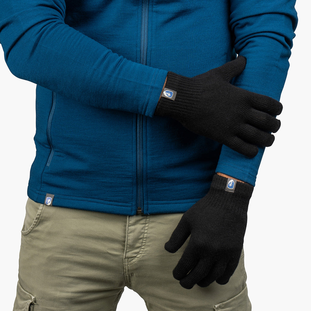 Person mit blauen Jacke trägt schwarze Merino Handschuhe Damen & Herren, Classic und fingerlos, von Alpin Loacker, zeigt sie gekreuzt für Outdoor-Aktivitäten.