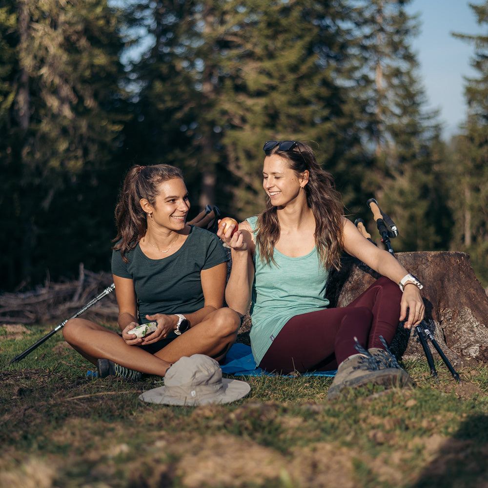 Zwei Frauen entspannen im Wald, tragen das Merino Tank Top Damen 150g/m2 von Alpin Loacker, ideal für Outdoor-Abenteuer, mit CORESPUN-Technologie für Komfort und Haltbarkeit.