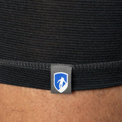 Nahaufnahme eines schwarzen, strukturierten Stretchstoffs über einem Bein, mit kleinem Schild-Logo, beschreibt Alpin Loacker Merino Boxershorts Herren 150 g/m² für Outdoor-Aktivitäten.