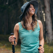 Frau mit Trekkingstöcken im Wald trägt das CORESPUN Merino Tank Top Damen 150g/m2, ideal für Outdoor-Aktivitäten, bietet optimalen Klima- und Tragekomfort.
