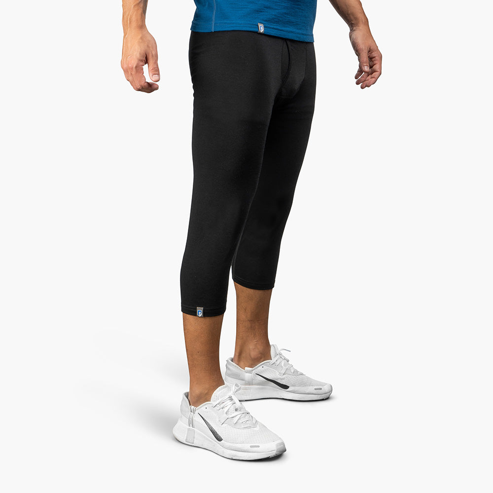 Herren in schwarzen 3/4 Merino langen Unterhosen, ideal für Outdoor-Aktivitäten. Kombiniert mit weißen Laufschuhen, bietet CORESPUN-Technologie Komfort und Langlebigkeit.