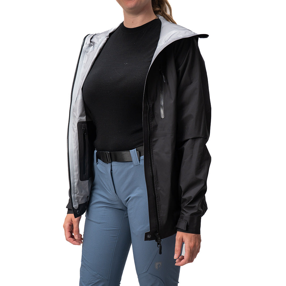 Person trägt eine offene 3 Lagen Damen Hardshell Regenjacke mit grauem Futter über schwarzem Shirt und blauen technischen Hosen. Perfekt für Outdoor-Aktivitäten.