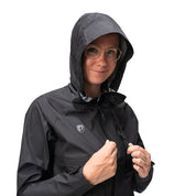 Person trägt schwarze 3 Lagen Damen Hardshell Regenjacke mit Kapuze und Logo, hält den Reißverschluss. Ideal für vielseitige Outdoor-Aktivitäten, wasser- und winddicht.