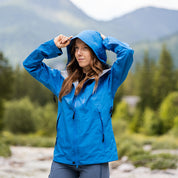 Person im Freien mit blauer 3 Lagen Damen Hardshell Regenjacke, passt Kapuze an, ideal für Outdoor-Aktivitäten, wasserdicht und atmungsaktiv.