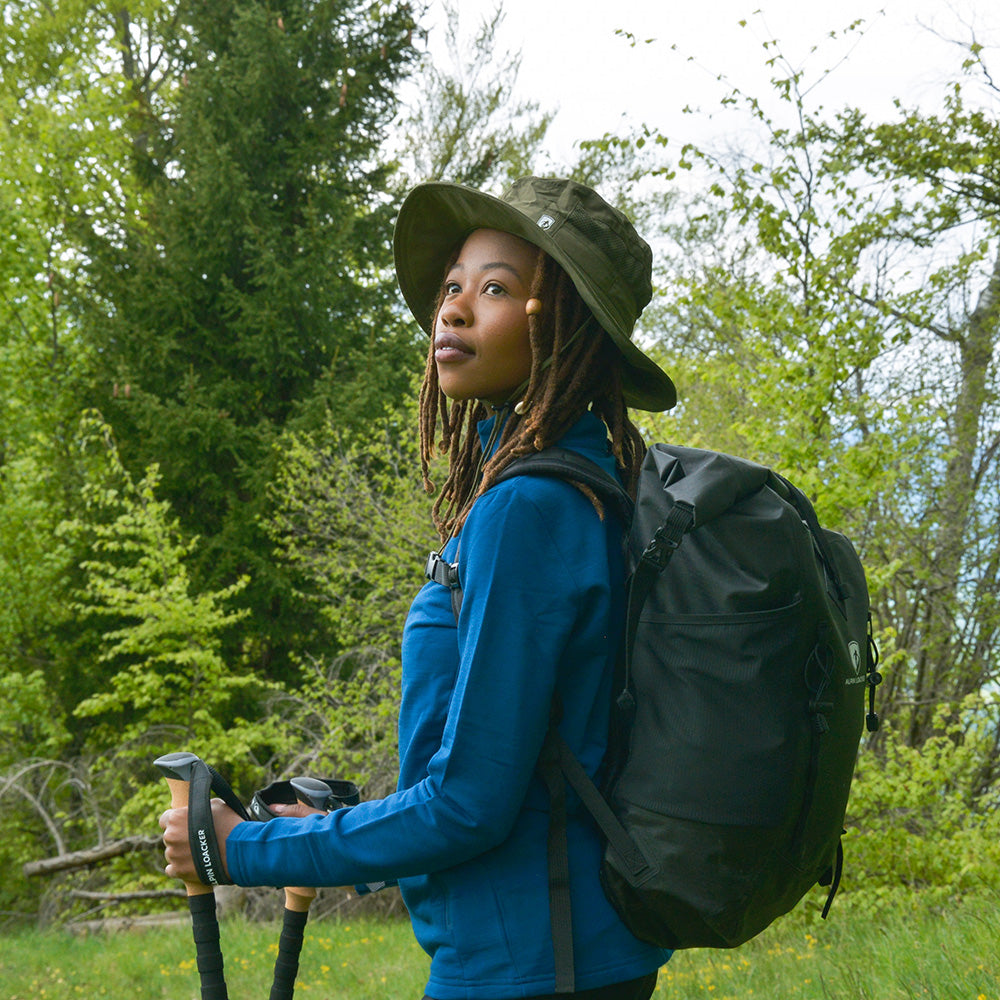 Person mit Sonnenhut mit UV Schutz Unisex, Trekkingstöcken und Rucksack im Wald. Idealer Begleiter für Outdoor-Aktivitäten, leicht und nachhaltig aus recyceltem Material.