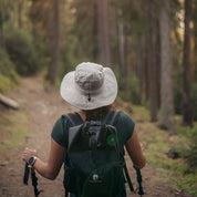 Wanderer mit Alpin Loacker Sonnenhut auf Waldweg, UV-Schutz und recyceltes Material, ideal für Outdoor-Aktivitäten.