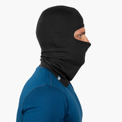Person mit snug schwarzer Merino Sturmhaube und blauem Langarmshirt, perfekt für Outdoor-Abenteuer; ergonomische Passform, ideal unter Helmen.