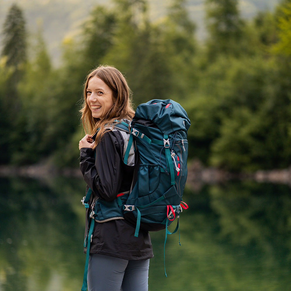Frau mit 35 Liter Wanderrucksack von Alpin Loacker, bereit für Abenteuer am waldbesäumten See, zeigt Funktionen für Komfort und Nachhaltigkeit bei Outdoor-Aktivitäten.