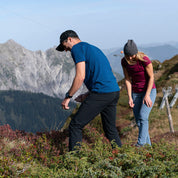 Zwei Wanderer inspizieren Sträucher am Berghang, tragen Softshell Wanderhose Herren, ideal für Trekking, leicht, flexibel, mit praktischen Reißverschlusstaschen, perfekt für Outdoor-Abenteuer.