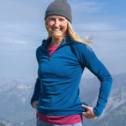 Person trägt das Merino Langarmshirt mit Zip Damen 230g/m2 in Berglandschaft, ideal für Outdoor-Abenteuer durch atmungsaktive, geruchsresistente Merinowolle.
