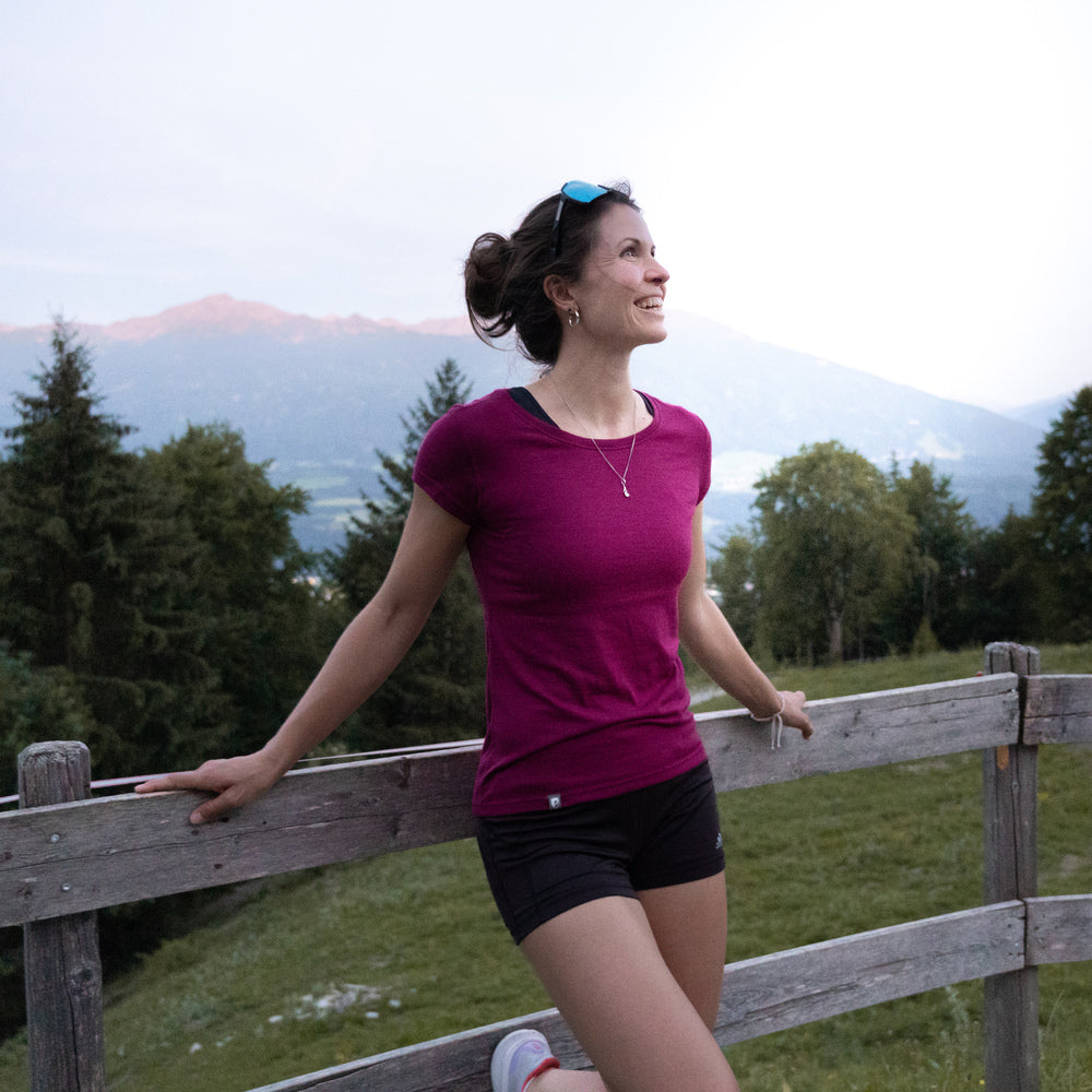 Frau lehnt am Zaun, trägt Merino Coolmax T-Shirt Damen 150 g/m2. Ideal für Outdoor-Aktivitäten, bietet Komfort und Funktion durch Merinowolle und Coolmax-Technologie.