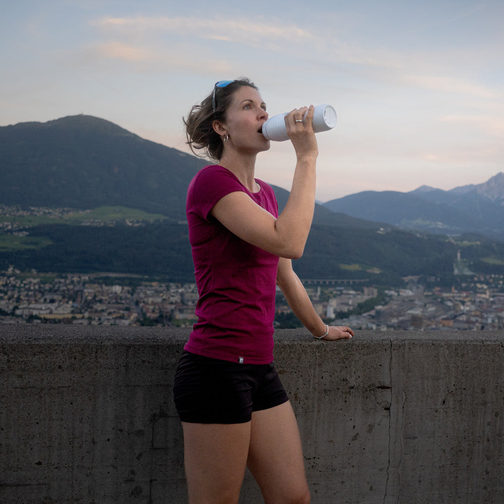 Frau mit Merino Coolmax T-Shirt Damen 150 g/m2 trinkt aus Trinkflasche, ideal für Outdoor-Aktivitäten, bietet Temperaturausgleich und Komfort.