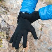 Person im Freien trägt einen blauen Isoliermantel und zieht Merino Handschuhe Damen & Herren, Classic und fingerlos, aus schwarzem Strick an oder aus.
