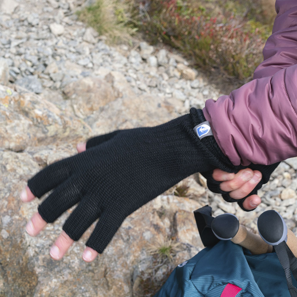 Person zieht fingerlosen Merino Handschuh an, ideal für Outdoor-Abenteuer. Sichtbar: Trekkingrucksack mit Stöcken. Produkt: Merino Handschuhe Damen & Herren, Classic und fingerlos.