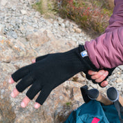 Person zieht fingerlosen Merino Handschuh an, ideal für Outdoor-Abenteuer. Sichtbar: Trekkingrucksack mit Stöcken. Produkt: Merino Handschuhe Damen & Herren, Classic und fingerlos.